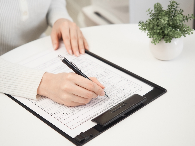 Person schreibt mit Kulli auf ein Formular in einer Kladde.