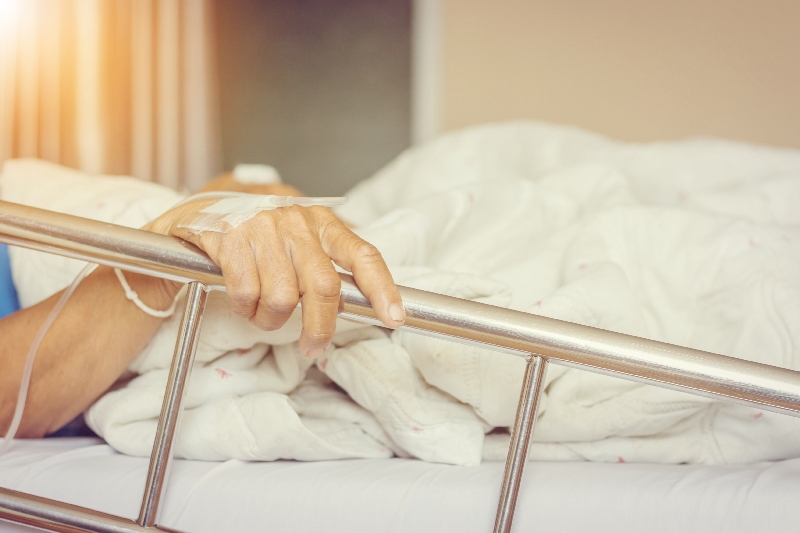 Pflegepatient liegt im Bett und hält sich an der Stange fest.