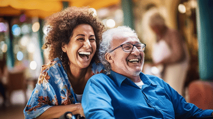 Afro-deutsche Pflegefachkraft schiebt ihren senioren Pflegekunden im Rollstuhl. Beide lachen und strahlen,