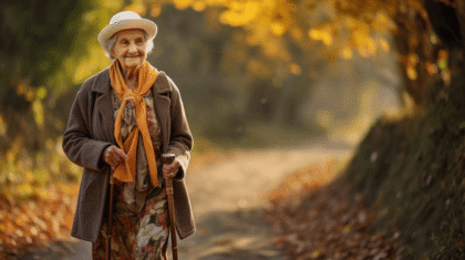 Ältere Dame mit zwei Spazierstöcken spaziert durch einen herbstlichen Wald.