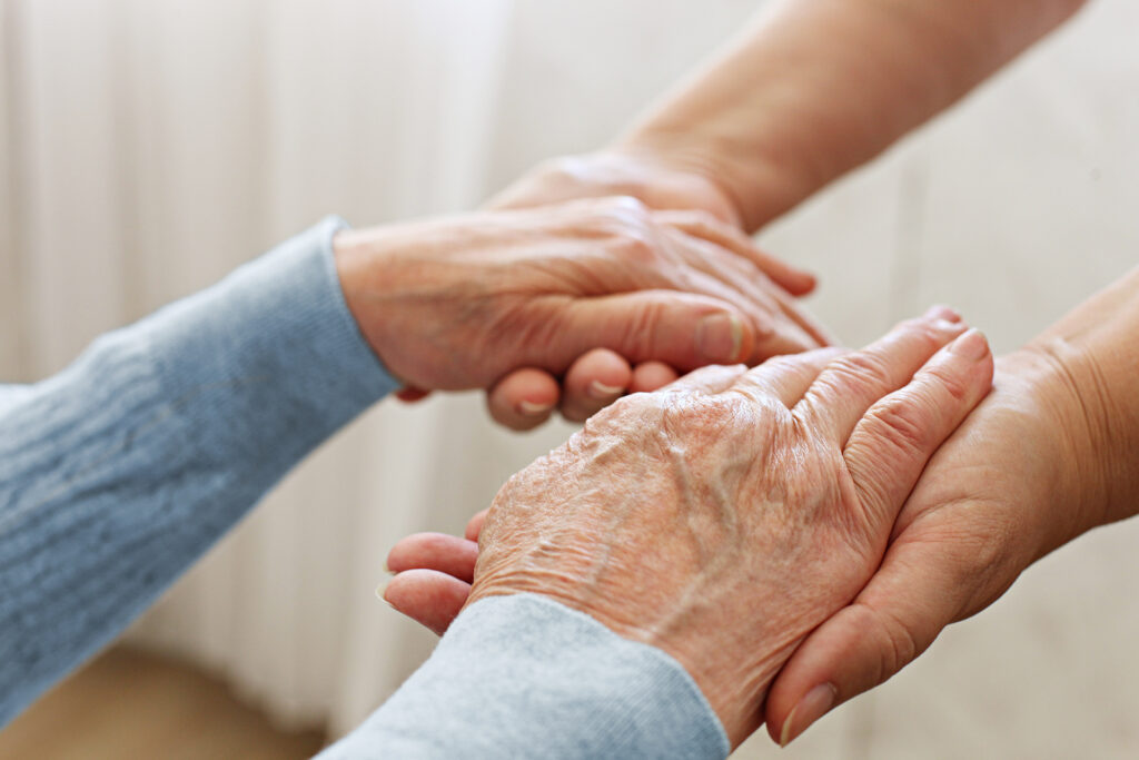 Eine Frau hält liebevoll beide Hände einer Seniorin und unterstützt diese mit Seelsorge.