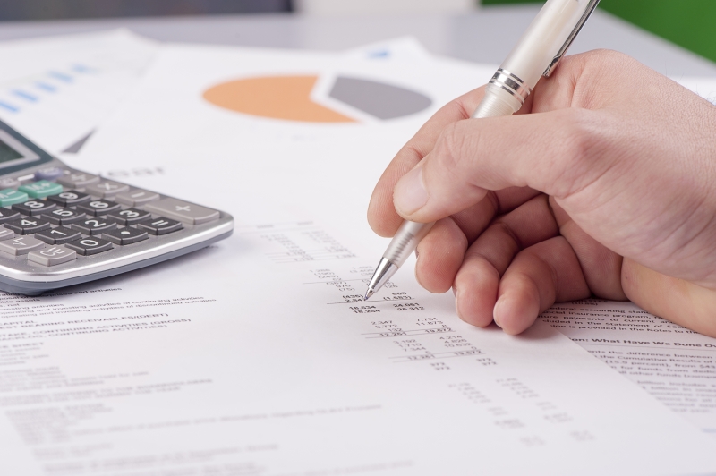 Ein Buchhalter überprüft die Zahlungseingänge auf einem Blatt Papier. Neben den Rechnungen liegt ein Taschenrechner.