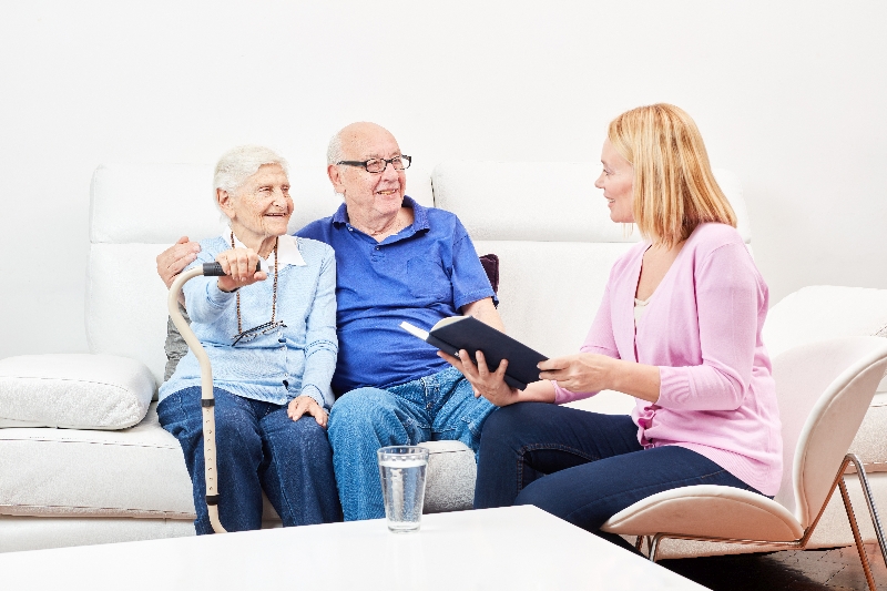 Seniores Ehepaar nehmen sich in den Arm auf einem Sofa und sind im gespräch mit einer Dame. Symbol: Beratungsgespräch