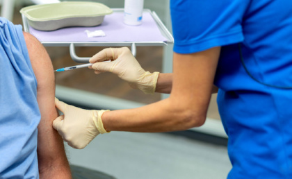 Pflegekraft impft eine Person in den Oberarm.