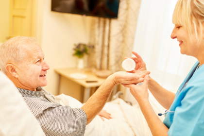 Seniorer Mann liegt im Bett und erhält seine Medikamente in die Hand.