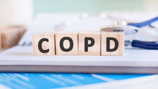 Im Zentrum des Bildes sind vier Holzklötze aufgestellt. Auf den Holzblöcken sind die Buchstaben COPD geschrieben. Links auf den Holzblöcken ist ein Stethoskop gelegt. Die Holzklötze liegen auf einem geöffnetem Ringbuch.