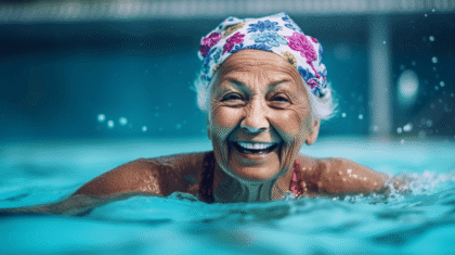 Ältere Dame mit Haube strahlend vor Lachen im Schwimmbecken.
