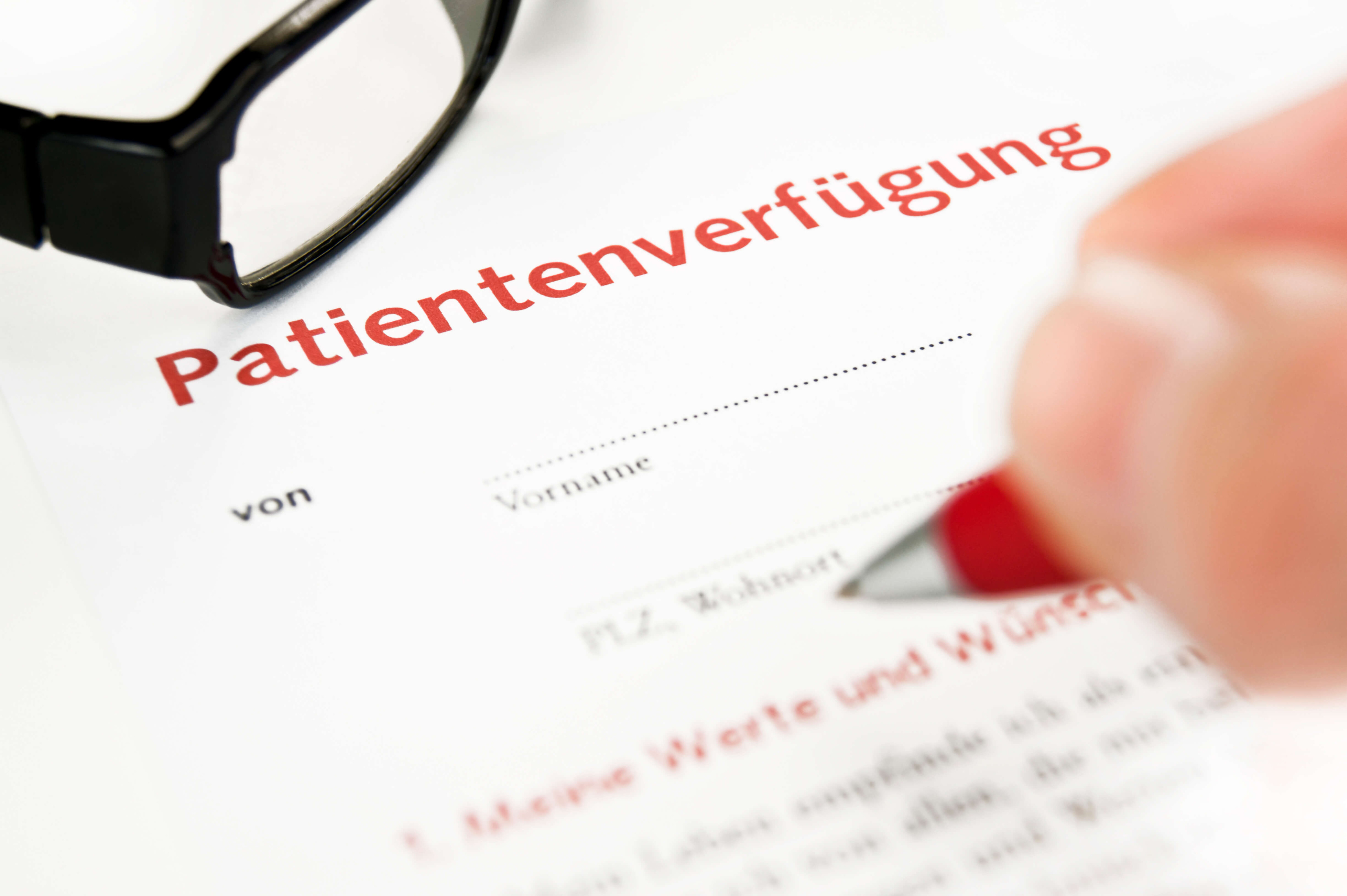 Ein Formular mit der Aufschrift "Patientenverfügung" wird von einem Menschen mit einem Kugelschreiber unterschrieben.