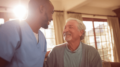 Junger Pfleger bei seinem Patienten. Im Hintergrund scheint die Sonne durch das Fenster.