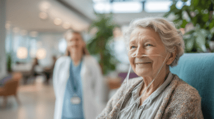 Seniorin mit Lungenfibrose. Im Hintergrund ist eine Pflegemitarbeiterin zu sehen.