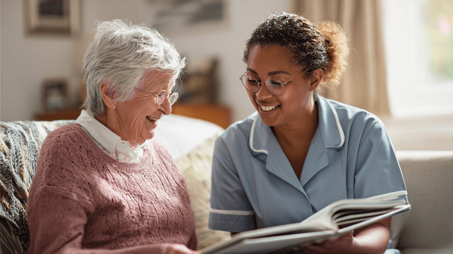 Pflegeperson liest Buch mit Seniorin auf dem Sofa