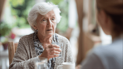 Seniorin mit Glas Wasser, Symbolbild für Schwierigkeiten bei Medikamentengabe
