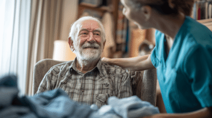 Pflegeperson legt Arm um dementen Mann im Sessel