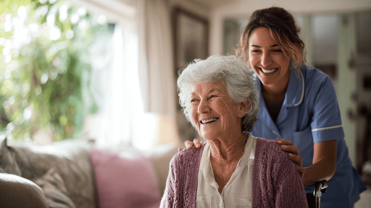 Pflegeperson im ambulanten Dienst ist bei alter Dame im Rollstuhl, beide lachen fröhlich