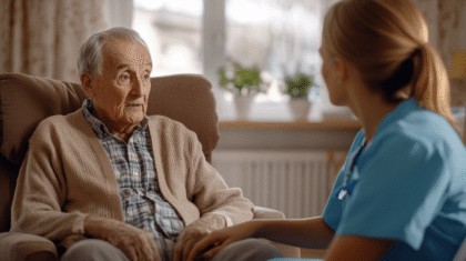 Junge Pflegerin legt ihre Hand empathisch auf das Knie eines verwirrten Seniors im Sessel