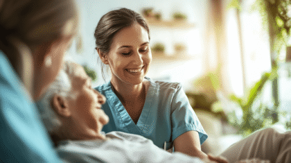 Pflegefachassistentin in der Altenpflege ist am Bett einer Seniorin und lächelt.